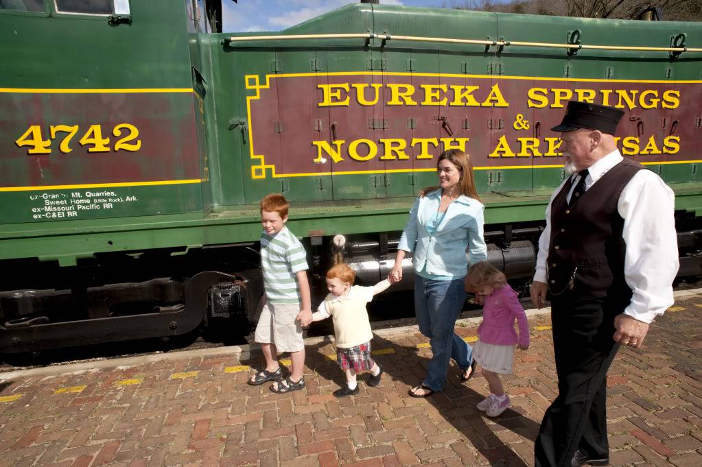 Train conductor leading woman and 3 children onto train 