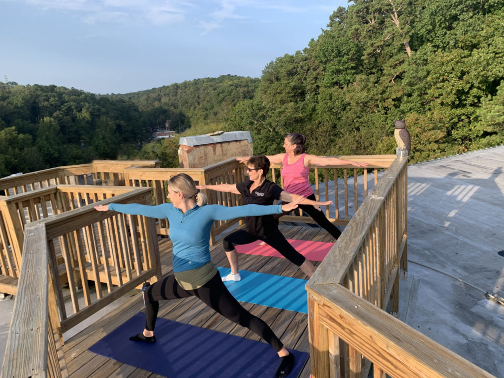 Three women in a yoga pose watching the sunrise from a rooftop