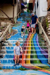 A colorful rainbow-painted staircase with children and an adult enjoying the outdoor art in Eureka S.