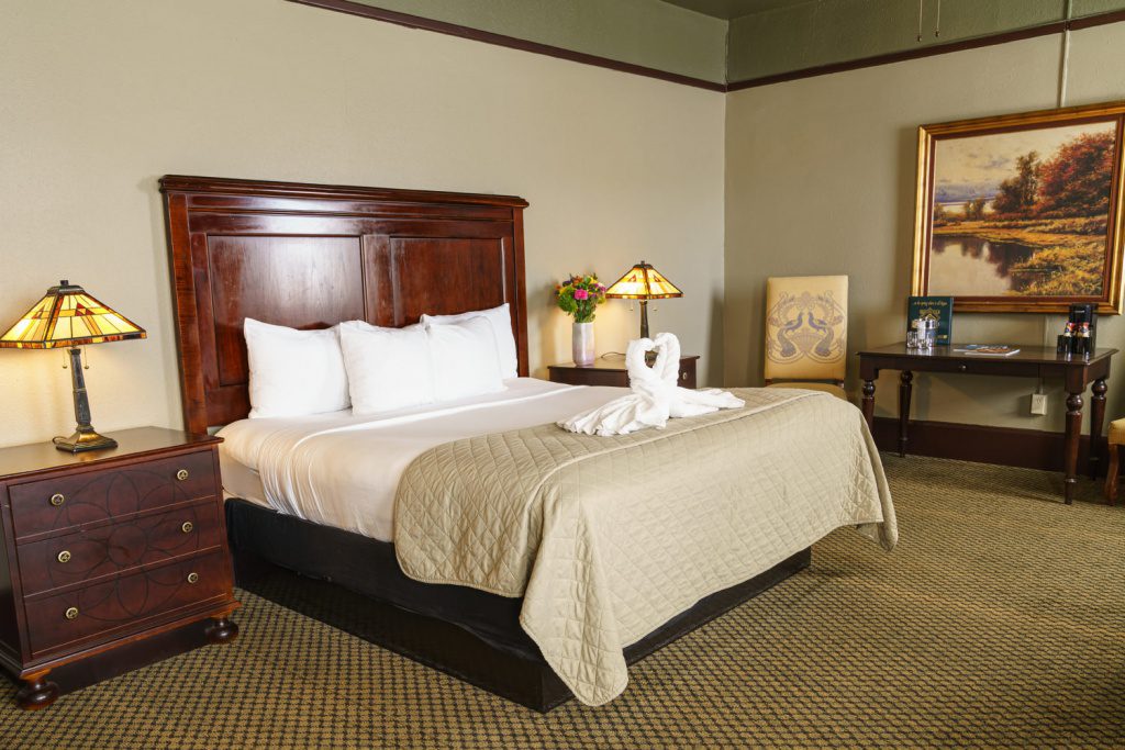 A cozy hotel room with a large bed, wooden headboard, and elegant decor.