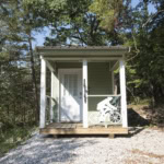 A small, charming green cabin with a white bicycle decoration in a wooded area, Eureka Springs.